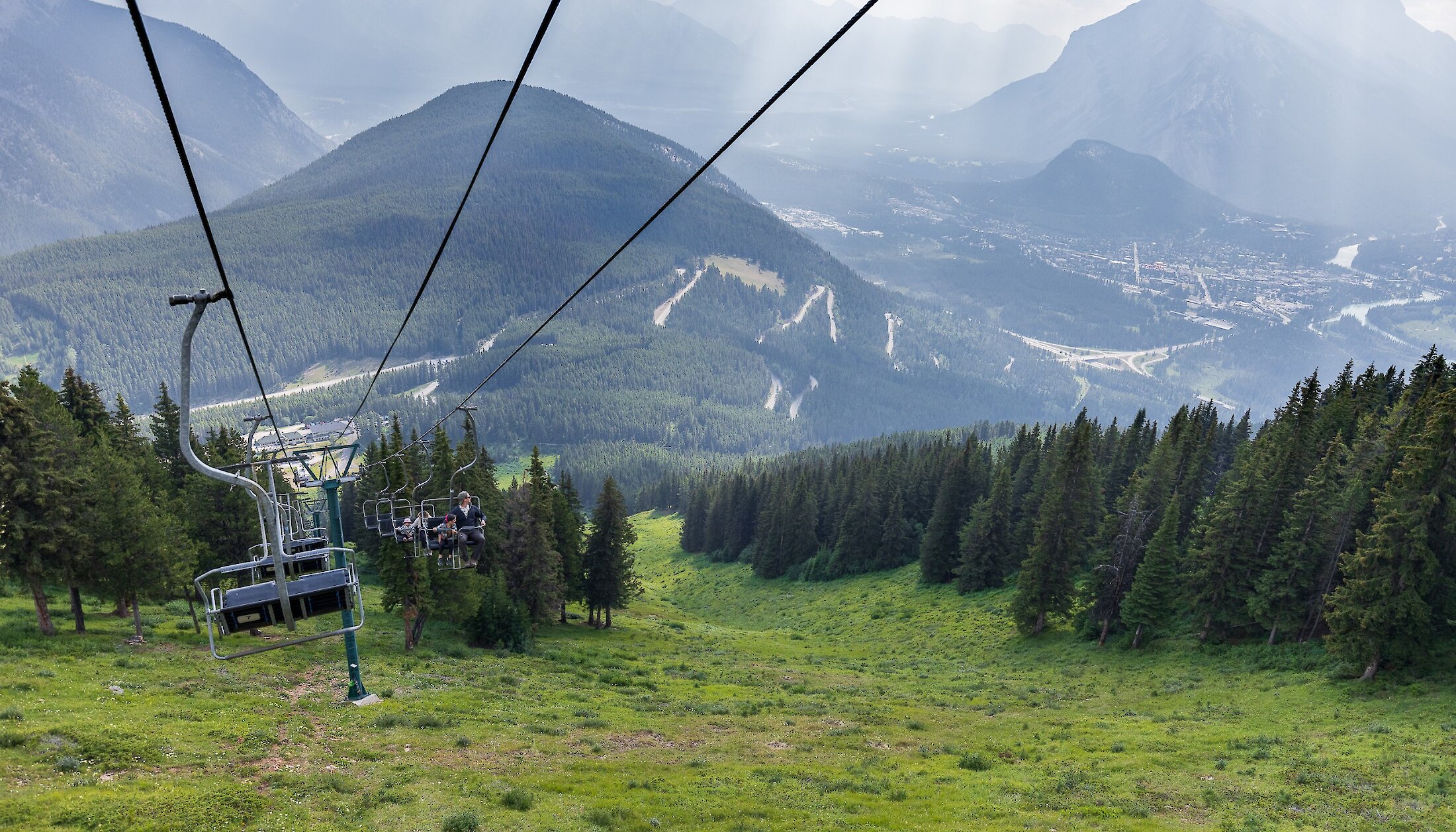 Two people riding up the Mount Norquay Chairlift with a mountain view background