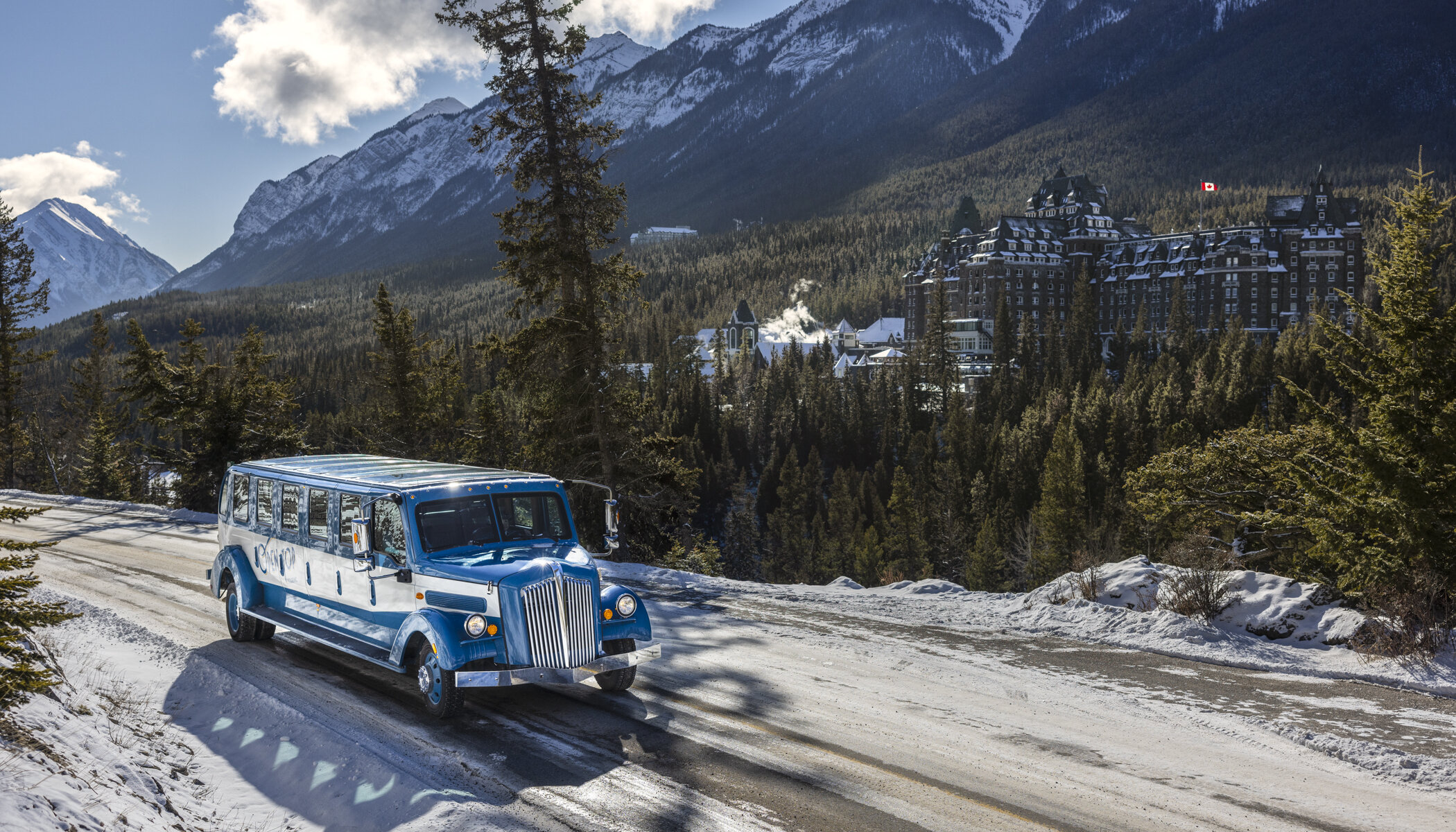 The Open Top Tour bus driving on Tunnel Mountain Road with a view of the Fairmont Banff Springs