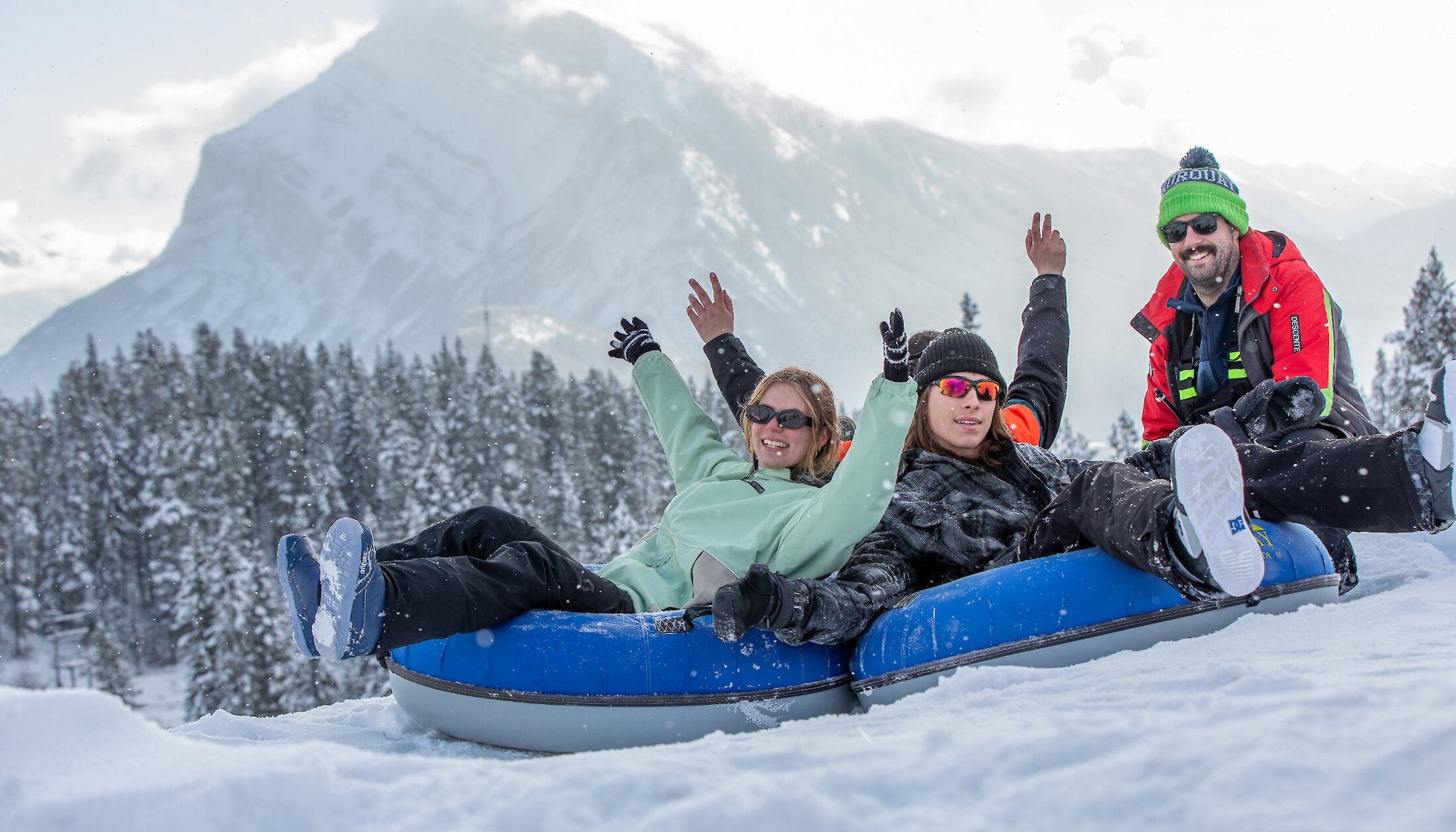 A group of friends snow tubing at mount norquay with a view of Mount Rundle