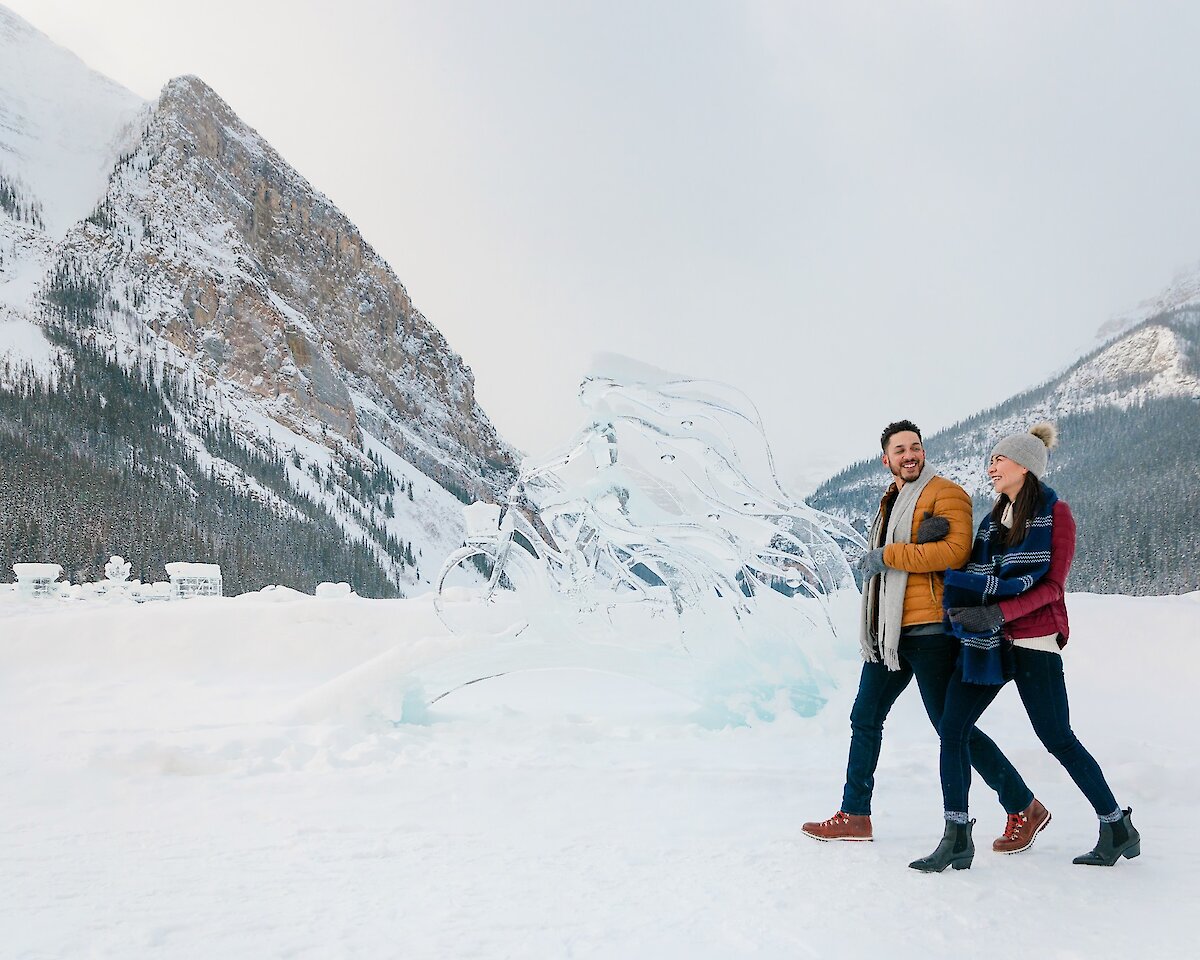 A couple walking along Lake Louise lake shore with the ice sculptures.