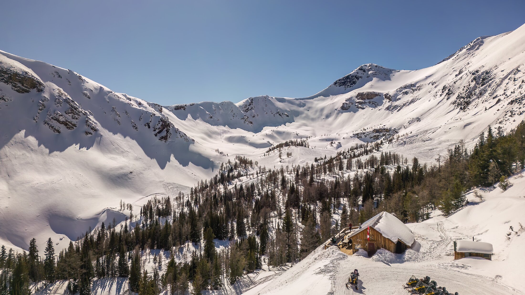 An aerial view of the paradise basin powder bowl and the cabin with snowmobiles