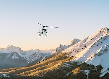 A helicopter flying over the rockies at sunset